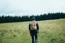 A young man walking up a hill with a backpack.