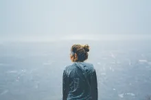 A young woman looking out over a cliff while it is snowing.