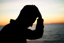 A silhouette of a man with his hand on his head.
