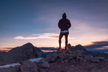 A person standing on top of a rocky hill watching the sunset.