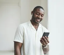 a man holding a phone and wearing earbuds while standing indoors