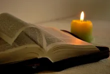 an open Bible beside a candle