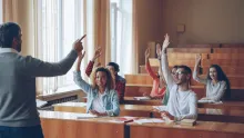 a group of students seated in a classroom and raising their hands