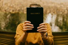 Person holding a Bible in front of their face