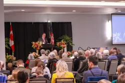 a group of people seated indoors and listening to a speaker on a stage