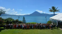 a large group of people outdoors with a body of water and mountain peak in the background