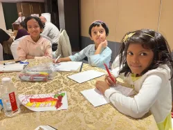 three children seated at a table and drawing on paper