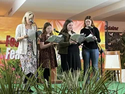 four ladies singing on a stage with plants in the foreground