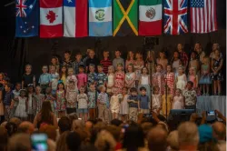 a children's choir on a stage underneath a variety of national flags