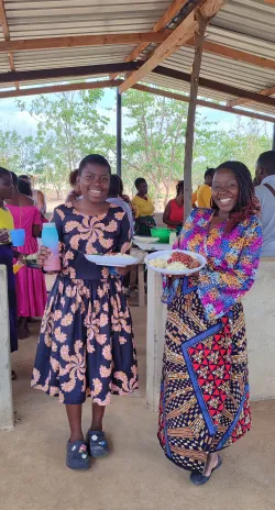 two women holding plates of food while standing underneath a picnic shelter