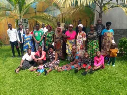 a group of people outside standing and sitting on the grass under palm trees