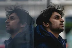 A man leaning against a shiny wall showing his reflection.