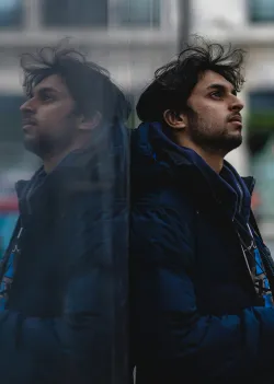 A man leaning against a shiny wall showing his reflection.
