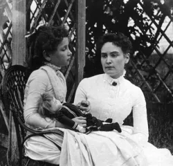 a woman and a girl sitting outside with a doll in a garden