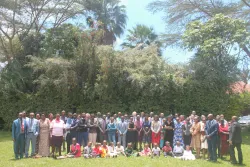 a large group of people outdoors on a green lawn with trees behind them