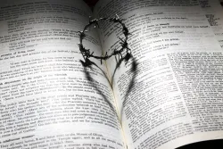 a crown of thorns casting a heart-shaped shadow on a Bible opened to a passage about Christ