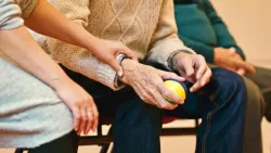 a woman's hands reaching out to comfort an elderly man seated beside her