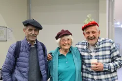 three smiling people standing indoors and wearing hats