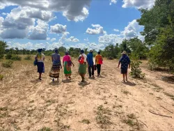 seven people walking outdoors in a dry field with a cloudy sky overhead