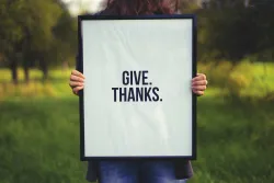 A person holding a sign that says: Give. Thanks.