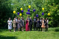 a group of young men and women standing outdoors and holding yellow and purple balloons