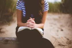 a woman sitting with folded hands on an open Bible