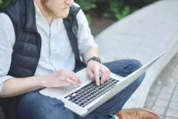 A man typing on a laptop on his lap.