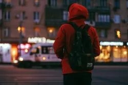 A person wearing a jacket and backpack walking in a city.