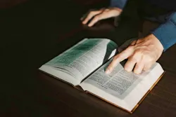 a hand pointing to a verse in an open Bible