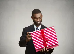 A man holding a wrapped gift looking at it.