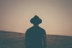 A man wearing a hat looking out over a grassy field.