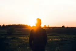 A person walking in a field with a sunset in front of them.