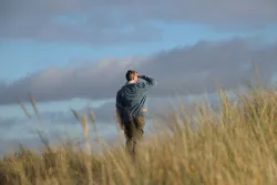 A man walking in a field looking at the clouds.