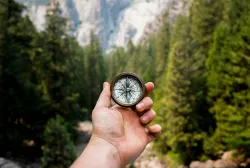 a hand holding a compass with mountains in the background