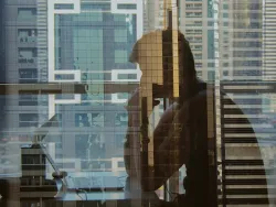 The reflection of man sitting and staring at his laptop computer.
