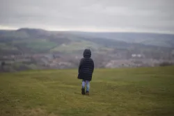 Child in black jacket walking on grass field during daytime.