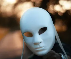 a white theater mask held in a hand from the shadows