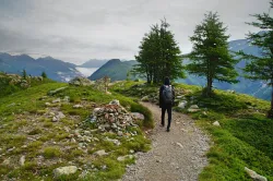 a man walking on a mountain trail looking out at the peaks in the horizon