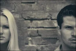 half of a woman's face and half of a man's face in grayscale separated by an expanse of brick wall