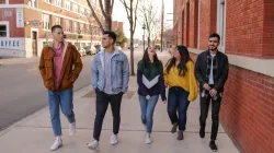 three young men and two young women walking on a city sidewalk