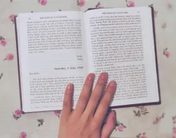 a book held open with a hand on a table covered with a flowered tablecloth