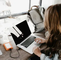 A woman seated with an open laptop and a backpack on the desk in front of her