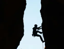 a silhouette of a woman climbing a rockface with another rockface behind her