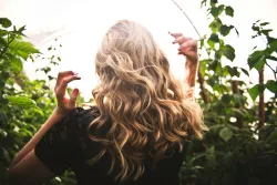 a woman's blond curly hair with hands gesturing to her head