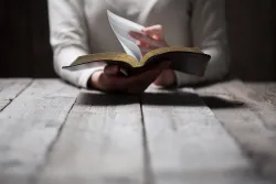 A person reading a Bible while sitting a table.