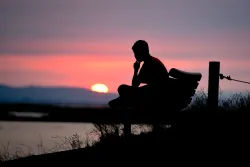 A person sitting on a bench with the sun setting.