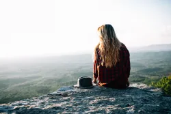 A young woman sitting on the edge of a rock.