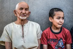 An old man (maybe the grandfather) and young boy sitting against a wall.