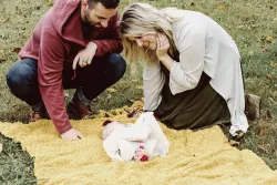 A dad and mom looking at their baby on a blanket.
