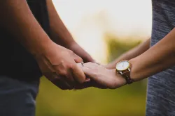 Photo of man and woman with wedding rings holding hands.